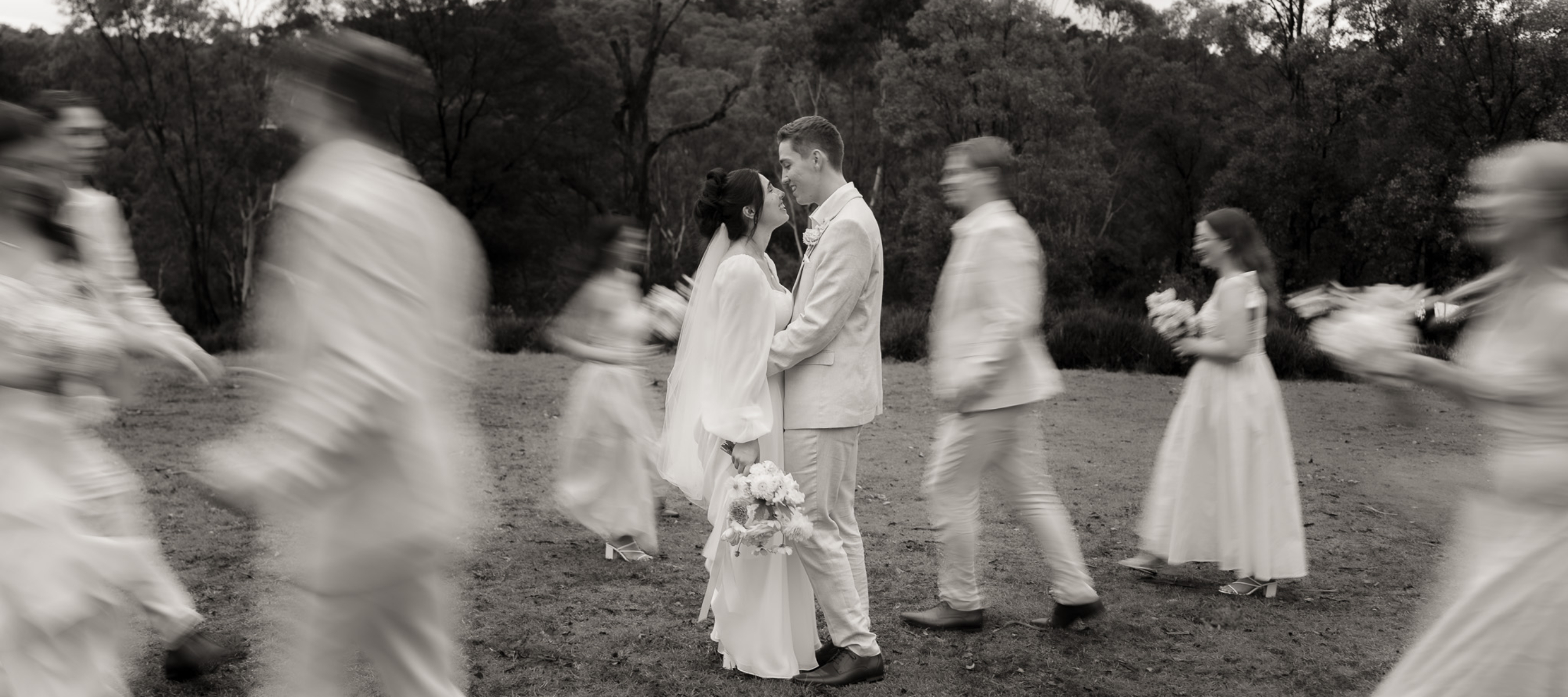 Bride and Groom hugging while bridal party move around them blurred. Black and White image.